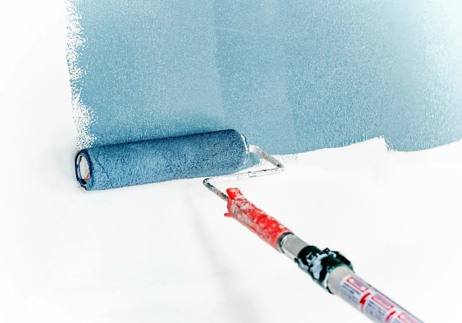 Eine Farbrolle zieht blaue Farbe über eine weiße Wand.